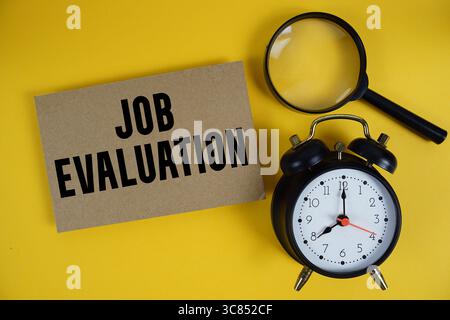 Texte d'évaluation du poste écrit sur papier avec loupe et réveil sur fond jaune Banque D'Images