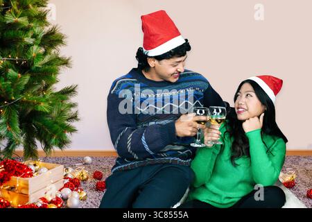 Heureux couple asiatique célébrant Noël avec chapeau de Père Noël, arbre de Noël, cadeaux, nourriture et boissons Banque D'Images