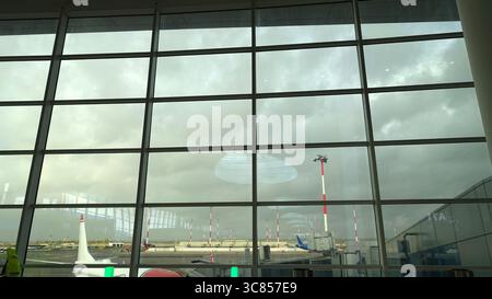 Un aperçu des avions et de l'extérieur d'un aéroport vu à travers la fenêtre de la salle d'attente par une journée très nuageuse. Banque D'Images
