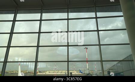 Un aperçu des avions et de l'extérieur d'un aéroport vu à travers la fenêtre de la salle d'attente par une journée très nuageuse. Banque D'Images