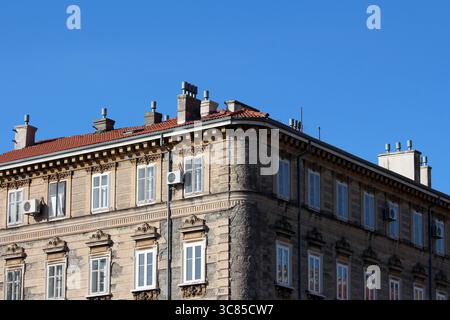 Un bâtiment en pierre de style européen de plusieurs étages avec des cadres de fenêtres ornés, un toit en tuiles rouges, de nombreuses cheminées sur le toit et des détails décoratifs extérieurs Banque D'Images