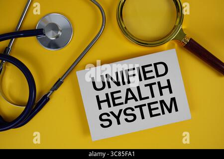 Texte du système de santé unifié sur carte papier avec stéthoscope plat sur fond jaune Banque D'Images
