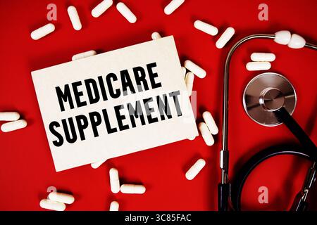 Texte du supplément Medicare écrit sur une carte papier avec stéthoscope et capsule de médicament sur fond rouge Banque D'Images