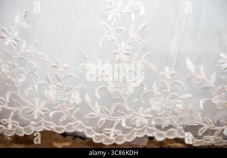 Un gros plan révèle un tissu blanc délicat orné de broderies florales complexes. Le savoir-faire met en valeur les détails fins et les textures, parfait Banque D'Images