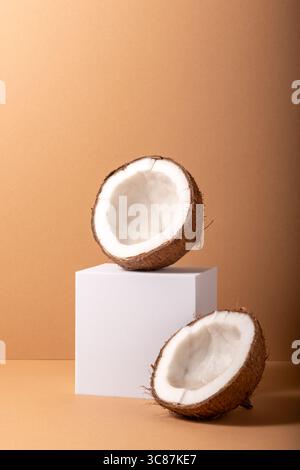 Concept minimal avec cube blanc et noix de coco craquelée sur fond marron. Banque D'Images