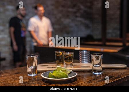 Videz les verres de tequila avec des quartiers de citron vert sur une table en bois dans un bar, vestiges d'une soirée. Vue rapprochée capturant l'atmosphère après les prises de vue. Banque D'Images