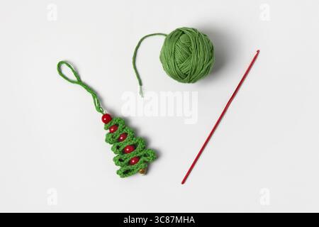 Arbre de Noël vert crocheté avec des perles rouges, un crochet à tricoter rouge, et une boule de fil vert sur un fond gris. Bureau d'artisanat et de tricot pour jouets et décorations de Noël Banque D'Images
