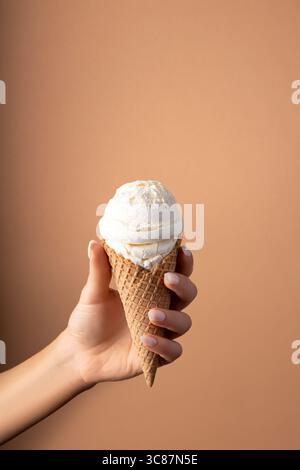 Cuillère à crème glacée blanche avec cône de crème glacée à la main sur fond lumineux. Concept estival minimal. Banque D'Images