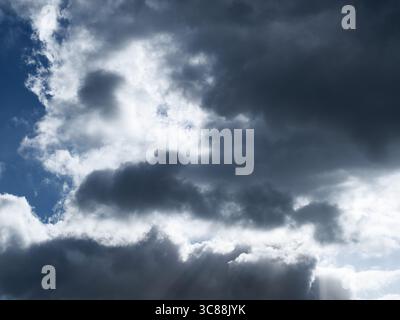 Un paysage urbain dynamique est affiché. Des nuages sombres et menaçants contrastent avec des taches de ciel bleu entrecoupées de nuages blancs brillants et moelleux pendant Banque D'Images