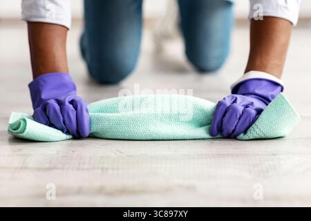 Un homme noir méconnu nettoie le sol, portant des gants en caoutchouc Banque D'Images