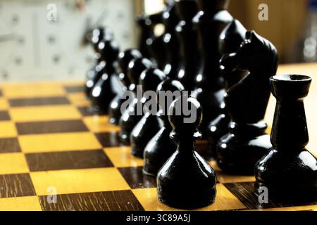 Vue rapprochée de pièces d'échecs noires disposées sur un échiquier en bois. Banque D'Images