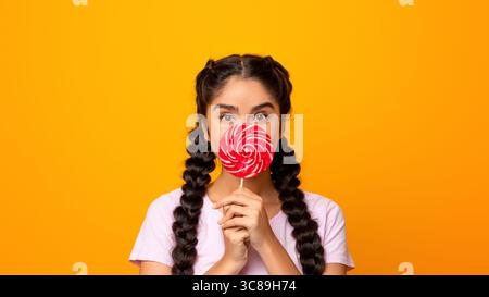 Femme indienne tenant une lollipop, couvrant la bouche avec des bonbons Banque D'Images