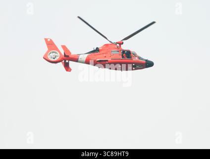Un membre de l'équipage regarde depuis une porte ouverte tandis qu'un dauphin Eurocopter de la Garde côtière survole l'action lors de la régate annuelle de la Stotesbury Cup. Banque D'Images
