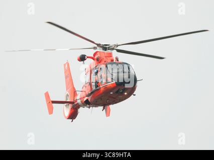 Un membre de l'équipage regarde depuis une porte ouverte tandis qu'un dauphin Eurocopter de la Garde côtière survole l'action lors de la régate annuelle de la Stotesbury Cup. Banque D'Images
