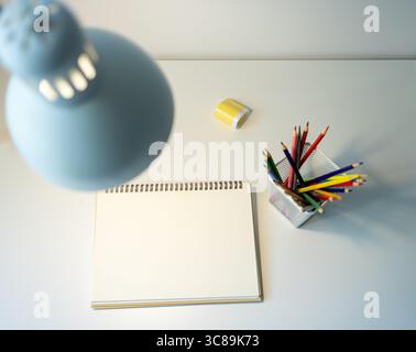carnet de croquis illuminé par lampe et jeu de crayons de couleur sur table, dessin et passe-temps, concept de retour à l'école Banque D'Images