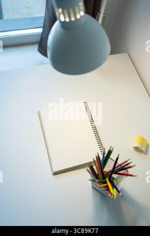 carnet de croquis illuminé par lampe et jeu de crayons de couleur sur table, dessin et passe-temps, concept de retour à l'école Banque D'Images