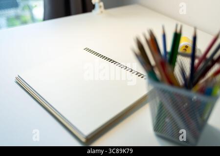 carnet de croquis illuminé par lampe et jeu de crayons de couleur sur table, dessin et passe-temps, concept de retour à l'école Banque D'Images