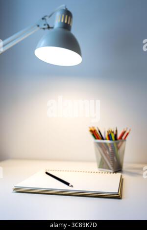 carnet de croquis illuminé par lampe et jeu de crayons de couleur sur table, dessin et passe-temps, concept de retour à l'école Banque D'Images