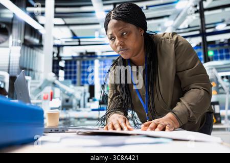 Femme noire vérifiant les machines de panneaux solaires et examinant la liste de contrôle sur les dossiers, jouant un rôle vital dans la production d'énergie renouvelable et la chaîne d'assemblage. Infrastructure de technologie solaire efficace. Banque D'Images