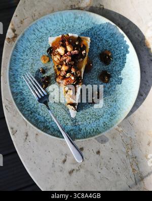 Vue de dessus d'une tranche d'un cheesecake crémeux classique avec une sauce caramel et garnie de noix sur une assiette en céramique bleue. Banque D'Images