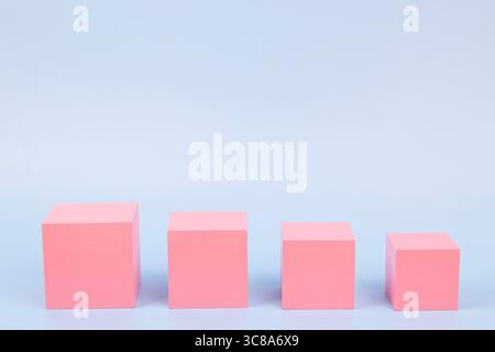 Quatre cubes en bois rose de différentes tailles disposés en rangée sur fond bleu clair. Vue de face Banque D'Images