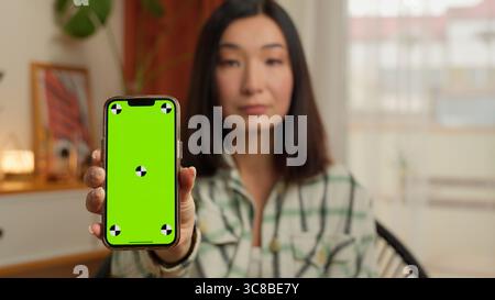 Sérieuse coréenne japonaise femme d'affaires femme d'affaires montrant l'écran vert de téléphone mobile à la caméra chroma portrait de femme asiatique fille chinoise maison Banque D'Images