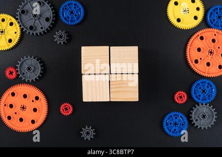 Vue de dessus de quatre cubes carrés en bois disposés dans une grille et entourés d'engrenages en plastique coloré sur fond noir. Représente l'apprentissage STEM, Innova Banque D'Images