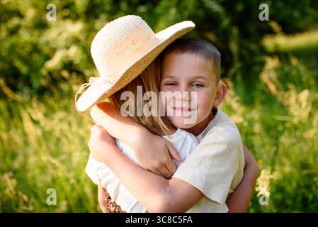 Frères et sœurs debout dans de grandes herbes au coucher du soleil. Fin des vacances d'été. Banque D'Images