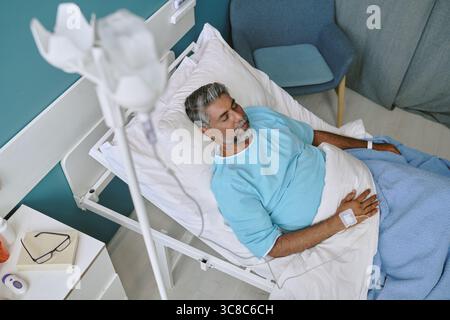 Homme biracial d'âge moyen au repos dans un lit d'hôpital en convalescence médicale Banque D'Images