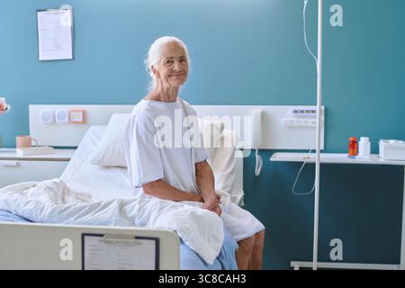 Portrait de femme caucasienne senior assise sur le lit d'hôpital souriant Banque D'Images