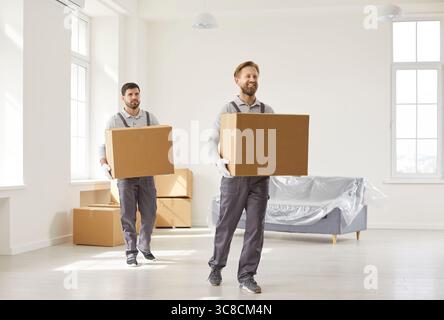 Deux déménageurs occupés transportant des boîtes en carton avec des effets personnels, travaillant dans le service de relocalisation Banque D'Images