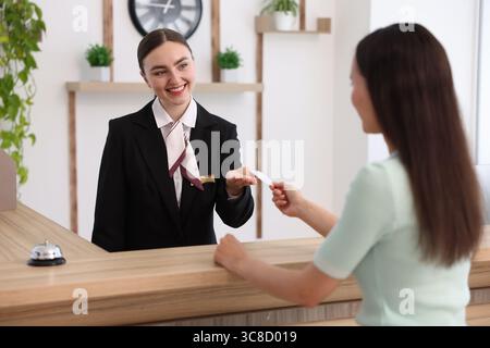 Réceptionniste souriant recevant la carte-clé de l'hôtel du client à la réception à l'intérieur Banque D'Images