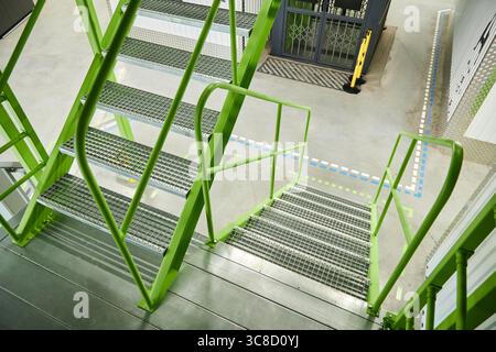 Escalier industriel moderne avec garde-corps en métal vert et marches grillagées Banque D'Images