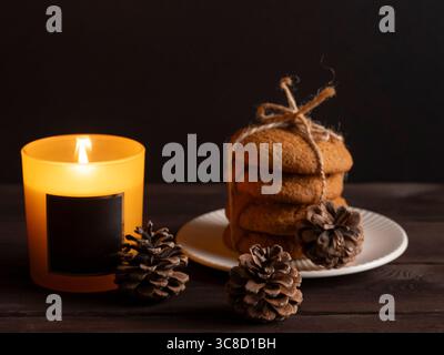 Biscuits rustiques et bougie brûlante avec pommes de pin sur la table en bois foncé Banque D'Images