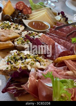 Le plateau de charcuterie gastronomique propose un assortiment de fromages, de charcuteries et d'olives, disposés artistiquement sur un plateau en bois. Tranches de pain garnies de pistaches Banque D'Images