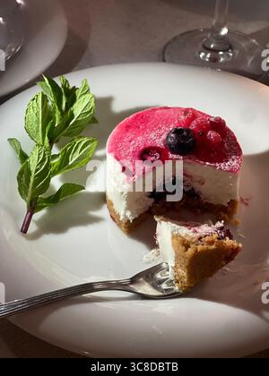 Tranche de cheesecake aux baies servie dans une assiette avec une fourchette et des feuilles de menthe fraîche. Le dessert vibrant dispose d'une garniture riche et crémeuse avec des baies, mis à un Banque D'Images