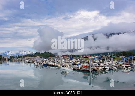 Bateaux amarrés dans le port avec de faibles nuages au-dessus de la ville et des montagnes par un matin brumeux sur la côte sud de l'Alaska. Valdez, Alaska, États-Unis Banque D'Images