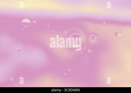 Texture fluide rose et jaune avec bulles d'huile flottantes. Bulles d'huile transparentes suspendues dans un fond fluide rose pastel et jaune doux. Banque D'Images