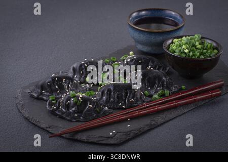 Boulettes de gyoza japonais, faites de pâte noire, gyoza noir, avec oignons verts et sauce, sur une assiette, gros plan Banque D'Images