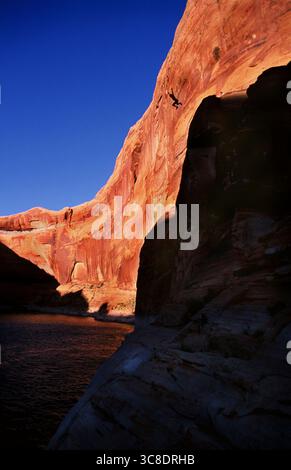 Un homme silhouette sautant d'une grande falaise dans les eaux du lac Powell à la fin de la journée. Banque D'Images