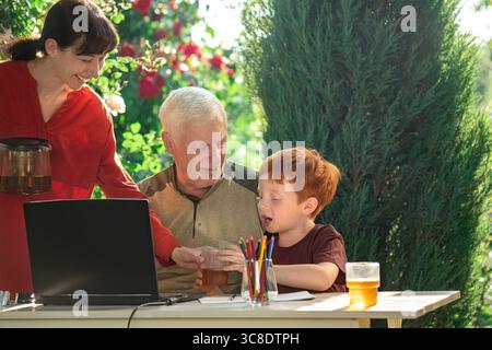 Famille assis à table avec ordinateur portable dans le jardin Banque D'Images