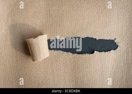 Trou déchiré dans du papier texturé brun sur fond gris foncé. Copier l'espace. Banque D'Images