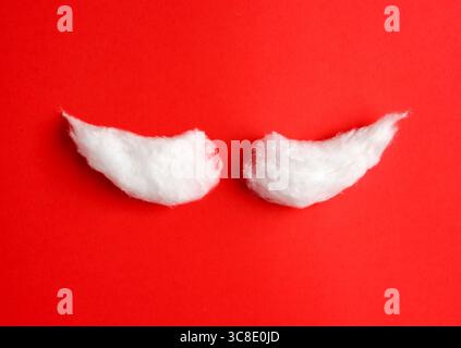 Forme de moustache du Père Noël en coton blanc doux sur un fond rouge vif. Concept de Noël ou de réveillon du nouvel an. Banque D'Images