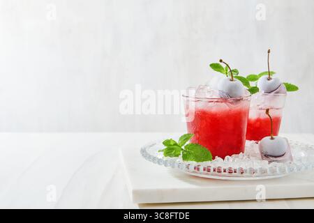 Cocktail rafraîchissant de cerise et de menthe dans un grand verre avec des glaçons écrasés, élégamment décoré avec des baies congelées, garniture de gel et de fleurs de jardin o Banque D'Images