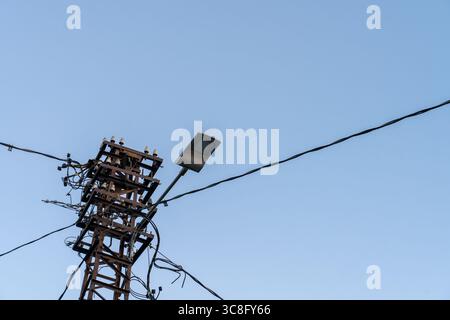Poteau électrique avec lampadaire et lignes électriques contre ciel bleu clair Banque D'Images