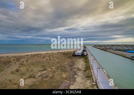 Canal se jetant dans le paysage marin, divisant le littoral sablonneux sous le ciel couvert, présentant un paysage côtier serein près d'Ostie, Rome Banque D'Images