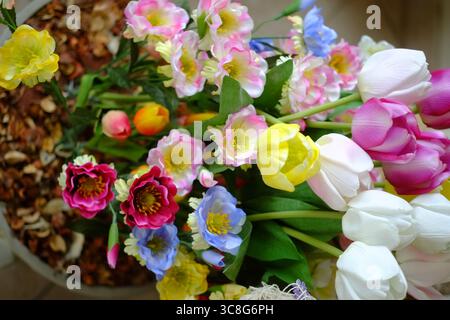 Tulipes artificielles vibrantes, lisianthus mélangeant des couleurs roses, violettes, blanches nichées dans un pot rustique au feuillage d'automne séché Banque D'Images