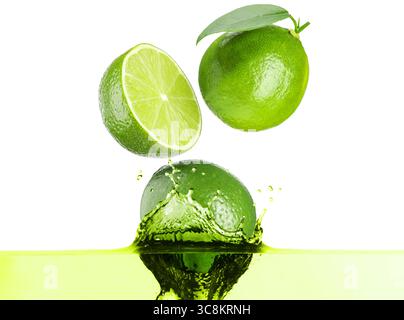 Citrons verts frais tombant dans la boisson éclaboussante sur fond blanc Banque D'Images