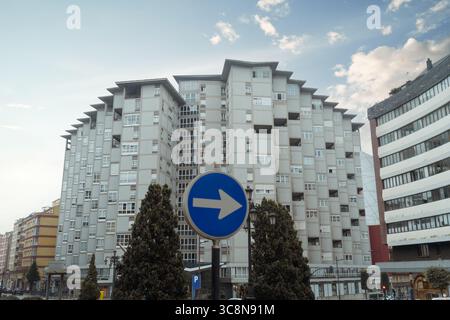Bloc d'appartements brutaliste symétrique domine l'horizon d'Oviedo, sa grille de béton pâle décalée par un panneau de signalisation floue bleu flèche droite dans le Forward Banque D'Images