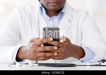 Connectez votre document pendant l'isolement. Médecin afro-américain en blouse blanche utilisant un smartphone, consultant des patients en ligne Banque D'Images